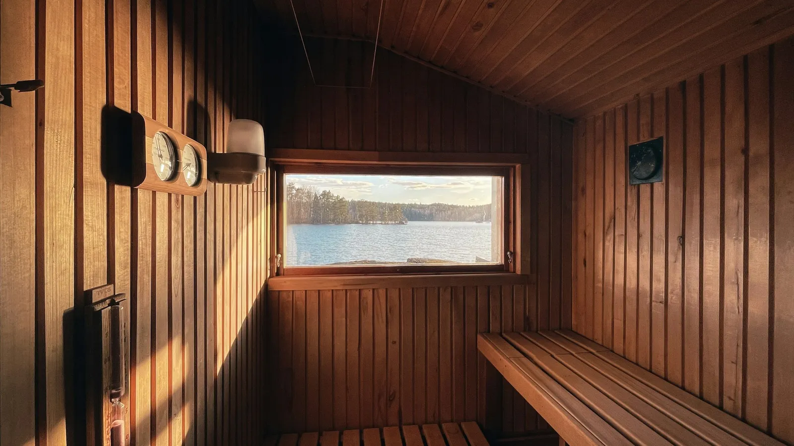 Niewielka domowa sauna z drewnianymi ławami, termometrem na ścianie i oknem